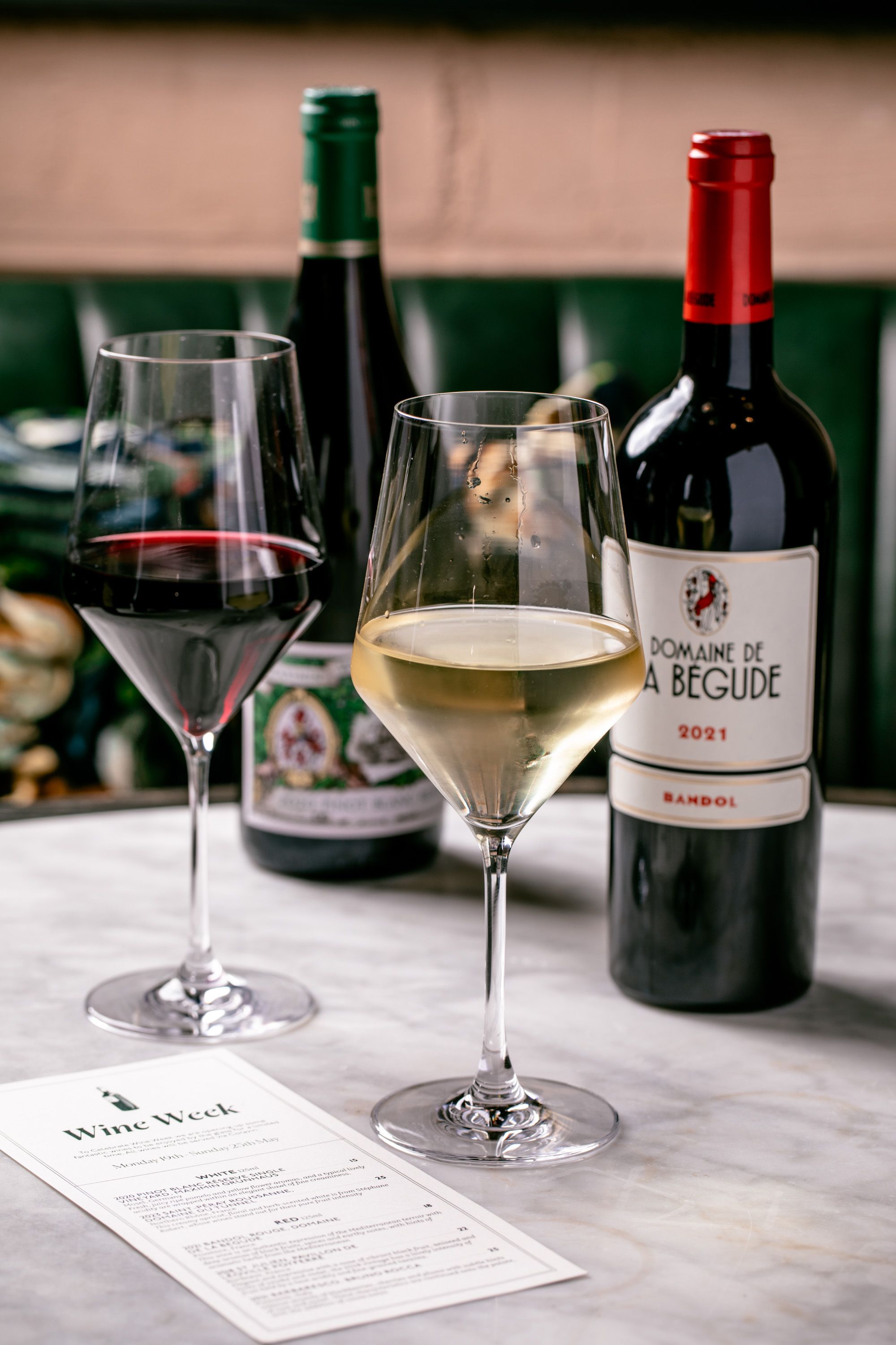 Glasses of red and white wine on a table with bottles in the background.