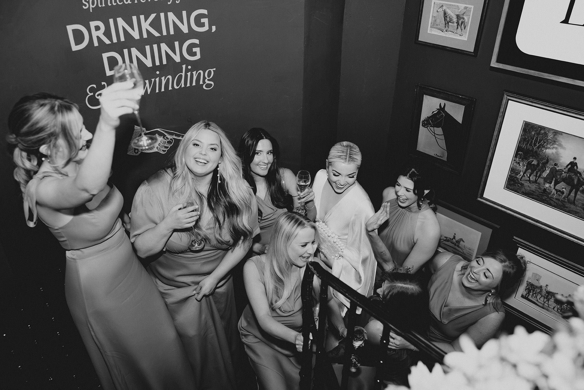 Bride and bridesmaids on staircase laughing and toasting.