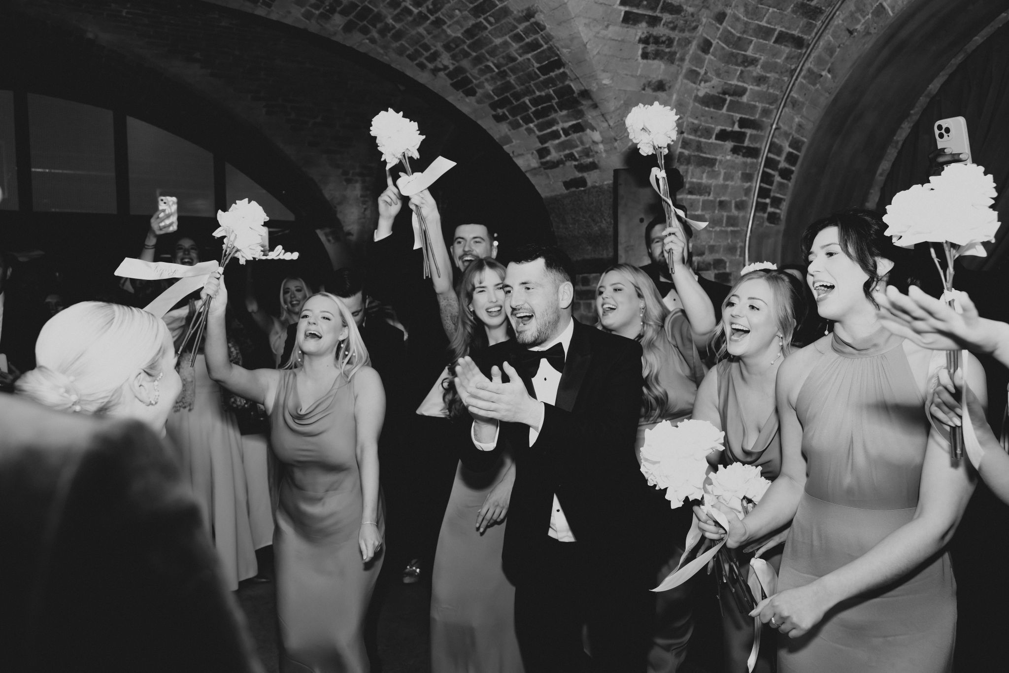 People cheering and celebrating at a wedding with flowers held in the air.